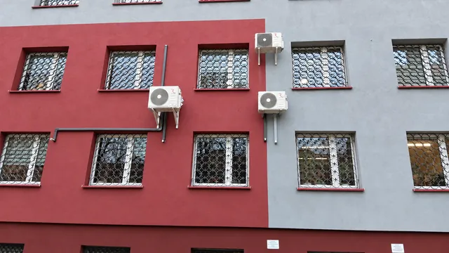 Trzy jednostki zewnętrzne klimatyzacji na czerwono-szarej elewacji.